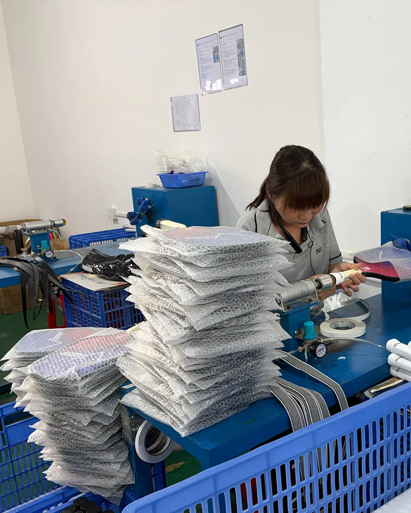 A skilled female artisan expertly wrapping a premium cushioned grip onto a pickleball paddle handle using a specialized rotary machine to ensure a smooth, secure fit.